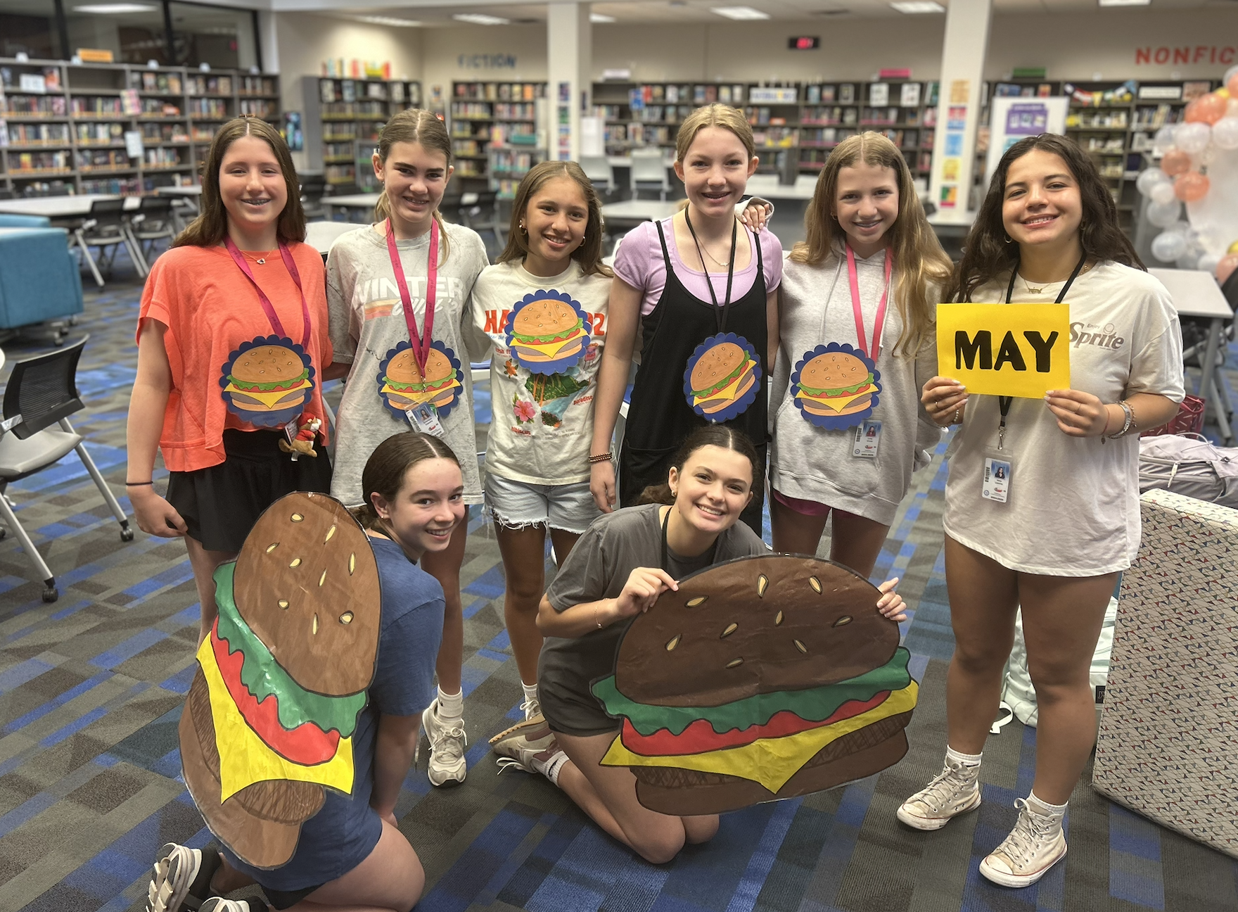 Students in the library wearing hamburgers and holding up May sign